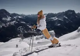 Kobieta na nartach z kijami na tle górskiego krajobrazu.