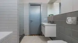 Nowoczesna łazienka z szarymi i białymi kafelkami, umywalką i drzwiami.