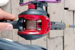 Zbliżenie na kołowrotek wędkarski z nawiniętą plecionką, ręka trzyma uchwyt.