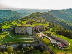 Forteca na wzgórzu, otoczona zielenią, z widokiem na góry. Srebrna góra trasa zaprasza do odkrywania historii.