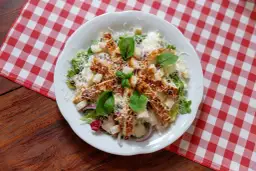 Sałatka Cezar z kurczakiem, grzankami i parmezanem na białym talerzu.