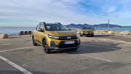 Dwa złote Dacia Sandero Stepway na tle morza i gór. Dwa modele, różne silniki, gotowe na przygodę.