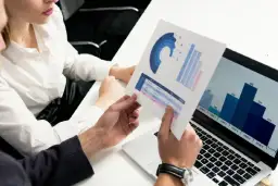 Dwie osoby analizują wykresy i dane na papierze i laptopie.