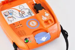 Pomarańczowy defibrylator AED z instrukcją użycia i wskaźnikami.