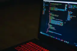 Kod HTML na ekranie laptopa z podświetlaną na czerwono klawiaturą. Widać fragmenty kodu, które mogą pomóc w nauce, jak zmienić kolor tła html.