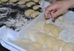 Ręka układa pierogi na tacy, posypanej mąką. Aby ugotowane pierogi się nie skleiły, warto je od razu po ugotowaniu delikatnie polać tłuszczem.