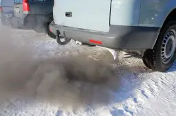 Ciemny dym wydobywa się z rury wydechowej samochodu na tle śniegu.