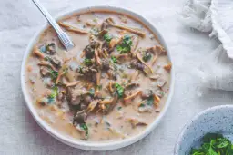 Kremowy sos z grzybów leśnych w białej misce, ozdobiony natką pietruszki.