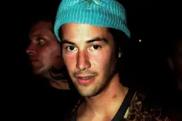 Młody Keanu Reeves w niebieskiej czapce, obok niego inny mężczyzna. Trudno zgadnąć, ile lat ma Keanu Reeves na tym zdjęciu.