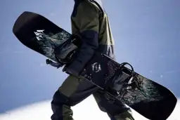 Osoba w zimowym stroju niesie dwa snowboardy z grafiką. Jeden z nich ma logo "JONES".