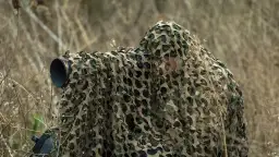 Fotografia przyrodnicza: ukryty fotograf z aparatem w kamuflażu czeka na idealny kadr wśród suchych traw.