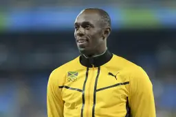 Usain Bolt w żółtej kurtce z flagą Jamajki i logo olimpijskim. Zastanawiasz się, jak szybko biega Usain Bolt?