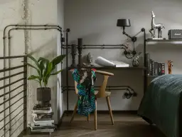 Industrialne wnętrze z czarnymi kablami na suficie, biurkiem, krzesłem z narzuconym szalem i łóżkiem.