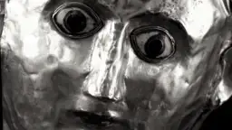 Zbliżenie na metalową maskę z wyrazistymi oczami i pofałdowaną twarzą.