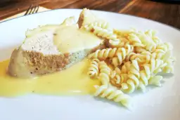 Kawałek mięsa w sosie z makaronem fusilli na białym talerzu.