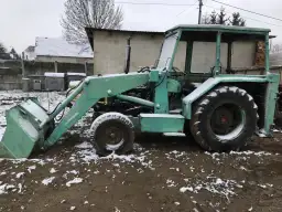 Zielona koparka Ostrówek stoi na błotnistym terenie, pokryta śniegiem.