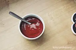 Miseczka z gęstym, czerwonym sosem barbecue i łyżeczką na drewnianym tle.