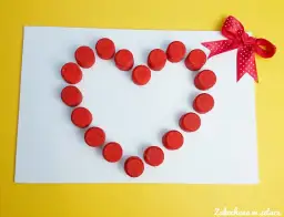 Urocza kartka walentynkowa diy z czerwonych koralików ułożonych w kształt serca, ozdobiona kokardką.