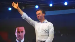 Mężczyzna w jasnej koszuli pozdrawia tłum. Na ekranie za nim widać twarz polityka, który mógłby mieć tyle lat, ile ma Bosak.