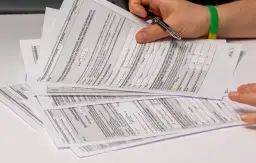 Dłoń z długopisem nad stosem dokumentów PIT, w tym formularzem PIT-28.
