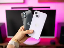 Dwa iPhone'y 14 w ręce, jeden ciemny, drugi fioletowy. Ich aparat jest gotowy do robienia zdjęć.
