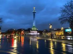 Wieczorny Paryż po deszczu. Kolumna Bastylii lśni w świetle latarni, a mokry asfalt odbija światła miasta.