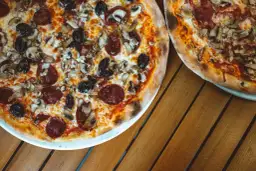 Dwie pizze z bogactwem składników na wierzchu: salami, pieczarki i czarne oliwki. Idealne na wspólny posiłek.
