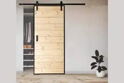 Drewniane drzwi przesuwne, składane z desek, z czarną klamką i prowadnicą, zasłaniające szafę z ubraniami i butami.