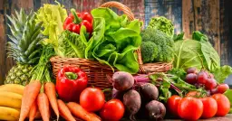 Koszyk pełen świeżych warzyw i owoców, idealnych na dietę owocowo warzywną: ananas, banany, marchew, papryka, pomidory, buraki, sałata, brokuły, kapusta, winogrona.