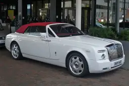 Biały Rolls-Royce Phantom Drophead Coupe z czerwoną, opuszczoną dachem, zaparkowany przed budynkiem.