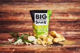 Reklamowa fotografia chipsów Big Snack o smaku zielonej cebulki, z ziemniakami i cebulką na drewnianym tle.