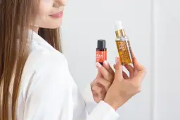 Kobieta prezentuje dwa produkty do pielęgnacji włosów, pokazując jak nakładać serum na włosy dla ich regeneracji i nawilżenia.