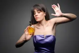 Kobieta w fioletowej sukni trzyma buteleczkę perfum.