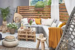 Przytulny taras w stylu boho z plecionymi meblami, poduszkami i paletowym stolikiem.