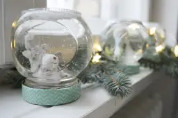 Urocza kula śnieżna diy z misiem w środku, otoczona gałązkami choinki i światełkami.