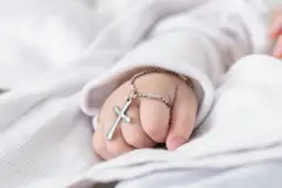 Dziecięca dłoń z krzyżykiem na srebrnym łańcuszku na białym tle.