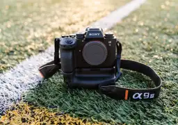 Profesjonalny aparat Sony Alpha 9 III, doskonały jaki aparat do filmowania, leży na sztucznej trawie.