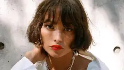 Krótkie, falowane włosy z grzywką to idealna fryzura do wysokiego czoła. Modelka ma wyraziste usta i delikatną biżuterię.