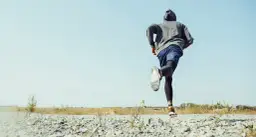 Mężczyzna w bluzie z kapturem biegnie po kamienistej drodze. To jego trening, jak przebiec maraton.