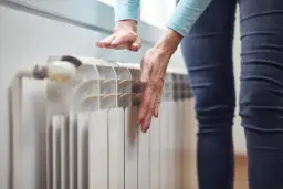 Dłoń sprawdza temperaturę grzejnika, który nie grzeje na dole.