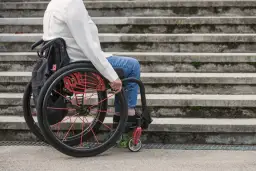 Osoba na wózku inwalidzkim przed schodami. Umiarkowany stopień niepełnosprawności a emerytura – ważna kwestia dla wielu osób.