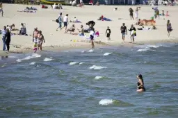 Plaża pełna ludzi, a w wodzie kąpie się kobieta. Warto sprawdzić, ile stopni ma Bałtyk latem, by móc cieszyć się takimi widokami.