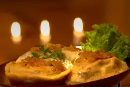Pierogi z cebulką i natką pietruszki, podane z sałatą, na tle świec.