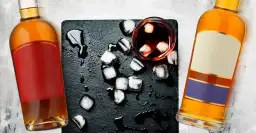 Dwie butelki, szklanka z lodem i ciemnym płynem. Ilustruje różnicę między whisky a whiskey oraz bourbonem a scotchem.