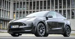Czarny Tesla Model Y stoi przed nowoczesnym budynkiem z cegły.