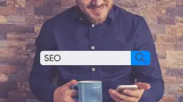 Mężczyzna z kubkiem kawy i telefonem szuka w internecie informacji o SEO. W pasku wyszukiwania widnieje hasło "SEO", sugerujące poszukiwanie w katalogu stron.