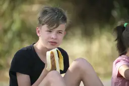 Chłopiec je banana. Zastanawia się, ile kalorii powinna jeść 13 latka, by mieć energię do zabawy.