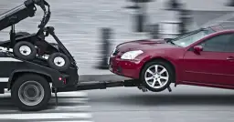 Czerwony samochód jest holowany przez czarną lawetę.