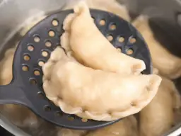 Gotowe pierogi z serem na łyżce cedzakowej, gotujące się w garnku. Idealne, by pokazać, jak zrobić pierogi z serem.