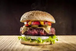 Parujący, soczysty burger z serem, warzywami i sosami na drewnianym blacie.
